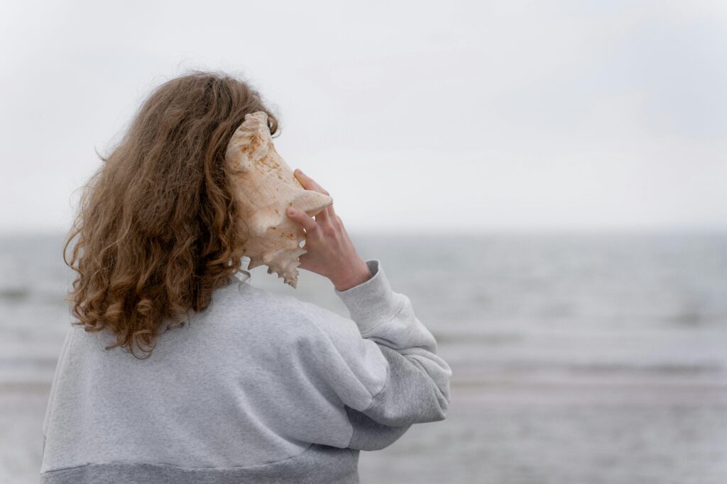 A young woman listens to a seashell by the ocean. Peaceful coastal scene.