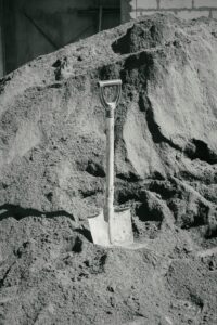 A solitary shovel upright in a massive sand pile, representing construction and labor.
